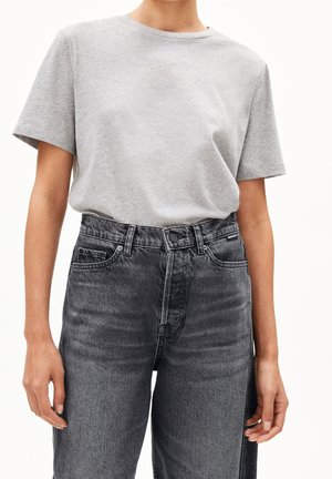 Personne portant un t-shirt uni gris clair à manches courtes, rentré dans un jean noir délavé taille haute avec poches avant et fermeture par boutons.