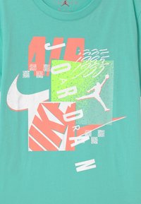 Turkusowa bawełniana koszulka z nadrukami w białym, neonowym różowym i zielonym kolorze, w tym tekstem oraz sylwetką Jordana.