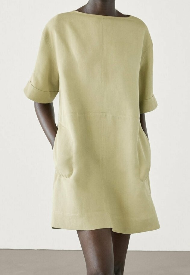 Robe vert olive clair à manches courtes, coupe ample, encolure arrondie et deux poches avant. Tissu lisse avec coutures minimales.