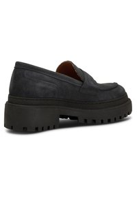 Svarta mocka slip-on skor med en kraftig, texturerad gummiyttersula. Har en avrundad tå och minimal sömnadsdetalj längs övre delen.