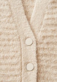 Beige gestrickte Strickjacke aus strukturiertem Stoff, V-Ausschnitt-Design und zwei hellen Knöpfen. Weiches, fusseliges Material mit sichtbaren Stichen.