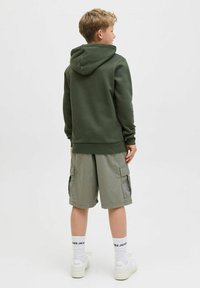 Olivno zeleni dukserica s kengurudžikom i podešavanjem za kapuljaču, uparen s svijetlosivim cargo šortsevima s bočnim džepovima. Bijele tenisice i čarape.