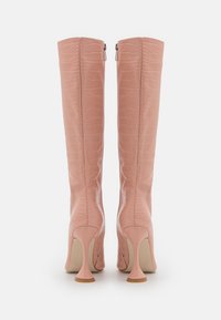 Para różowych skórzanych kozaków do kolan z teksturą krokodyla i wysokimi, wygiętymi obcasami, przedstawiona z tyłu na białym tle.