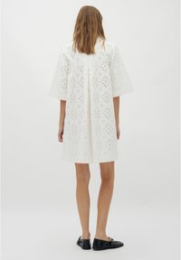 Biała sukienka w stylu eyelet z krótkimi rękawami, z kwiatowymi wycięciami i przeszyciem z tyłu. W zestawie z czarnymi płaskimi butami. Prosty design.