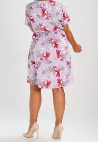 Kukkamekko, jossa on lilakantausta ja vaaleanpunaisia sekä valkoisia kukkia. Lyhyet hihat, joustava vyötärö ja polvimittainen helma. Yhdistetty paljain jaloin korkokenkiin.