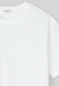 T-shirt blanc oversize avec un col rond et des manches courtes. Fabriqué en tissu souple avec une texture lisse. Étiquette de taille visible.