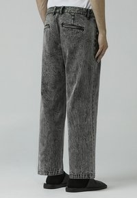 Grå denim jeans med avslappet passform, som har en falmet tekstur, to baklommer og glidelåsdetaljer på lommene.