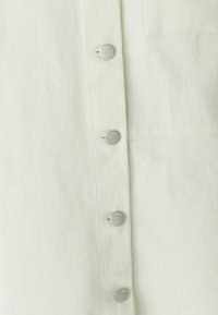 Světle zelená košile s texturovanou látkou, vybavená stříbrnými patentními knoflíky a náprsní kapsou. Jednoduchý, čistý design se šikmým žebrováním.