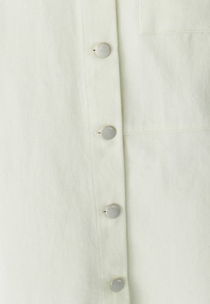 Světle zelená košile s texturovanou látkou, vybavená stříbrnými patentními knoflíky a náprsní kapsou. Jednoduchý, čistý design se šikmým žebrováním.