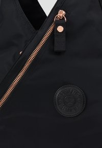 Black nylon bag featuring a rose gold zipper and a distinctive round black embossed logo. Smooth texture with a sleek design.