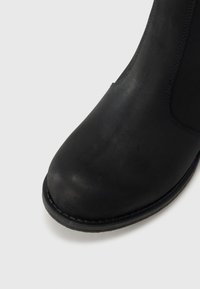 Fekete bőr bokacsizma lekerekített orral, sima felülettel és minimális varrással. A talp enyhén megemelt és texturált a jobb tapadás érdekében.