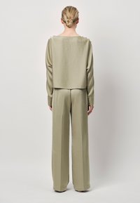 Tweedelig outfit in lichtgroene satin, bestaande uit een cropped lang mouwtop en een broek met wijde pijpen. Soepele textuur en minimalistisch ontwerp.