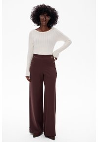 Szerokie brązowe spodnie z bocznymi kieszeniami i złotymi guzikami, zestawione z dopasowanym białym, prążkowanym topem z długim rękawem.