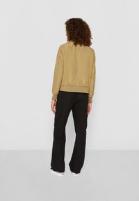 Khaki Bomberjacke mit gerippten Bündchen und Saum, die über eine glatte Textur und kontrastierende Netzpaneele verfügt, kombiniert mit schwarzen Cargo-Hosen.