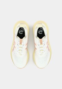Baskets blanches de sport avec une tige en maille respirante, des accents jaunes et des détails roses ; elles disposent d'une languette rembourrée et de semelles intérieures noires contrastantes.
