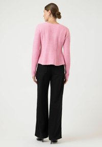 Różowy prążkowany sweter z długimi rękawami i dopasowaną talią, zestawiony z czarnymi, szerokimi spodniami z wysokim stanem. Tworzy kontrast kolorystyczny i fakturowy.