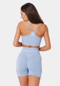 Gaiši zils sporta krūšturis ar regulējamiem siksnām un ribota faktūra, apvienots ar augsta vidukļa šortiem ar logo detaļām un gludu audumu.