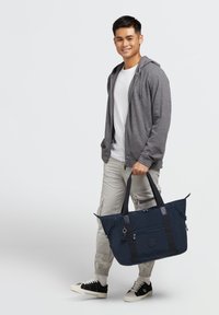 Granatowa torba na zakupy z zamknięciem na zamek, podwójnymi uchwytami oraz zewnętrznymi kieszeniami. Wykonana z trwałego materiału z akcentami w postaci detali metalowych.