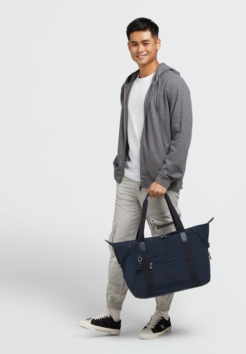 Granatowa torba na zakupy z zamknięciem na zamek, podwójnymi uchwytami oraz zewnętrznymi kieszeniami. Wykonana z trwałego materiału z akcentami w postaci detali metalowych.