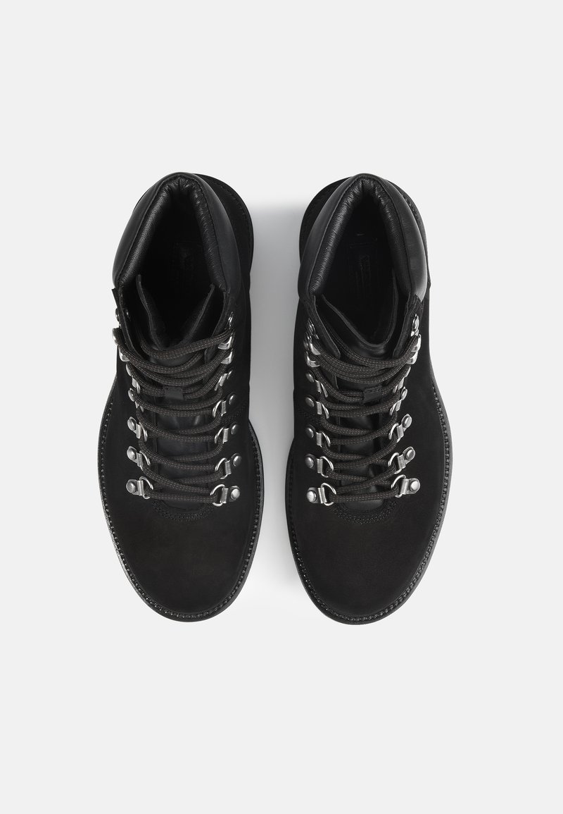 Zwarte leren wandelschoenen met metalen oogjes, gestructureerde veters en een rubberen zool met opvallende stiksels.