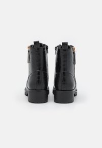 Bottines noires avec une texture crocodile brillante, dotées d'un talon carré, d'une fermeture éclair et d'une languette à l'arrière.