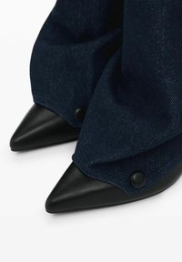 Cipele s visokim potpeticama sa šiljastim prstima, s osnovom od crne kože, s tamnoplavim traperom koji pada preko njih i crnim dugmadi kao ukrasom.