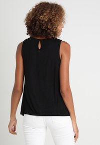 Svart ärmlös top i mjukt tyg, med en nyckelhålsöppning på baksidan och en avslappnad passform, i kombination med vita byxor.