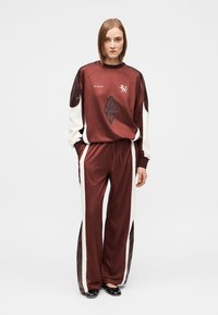 Survêtement bordeaux en tissu lisse comprenant un haut col rond avec des accents noirs et un motif losange, associé à un pantalon assorti avec des bandes latérales blanches.