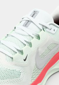 Világoszöld Nike futócipő, jellegzetes fehér hálós felsőrésszel, ezüst logóval és feltűnő rózsaszín talppal. A fűzők szépen meg vannak kötve.