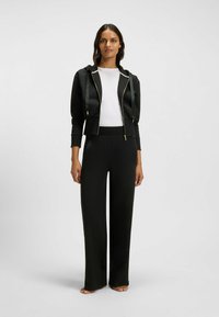 Zwarte cropped zip-up hoodie met gestructureerde trekkoorden, gecombineerd met losse zwarte broeken. Glad materiaal, minimalistische accenten en aansluitende boorden.