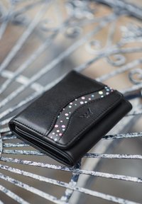 Black leather wallet with a curved design featuring a multi-colored polka dot pattern in the center, set on a decorative metal table.
