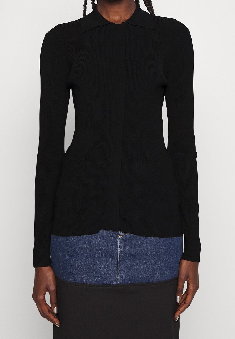 Svart ribbad stickad långärmad topp med krage, knappstängning och en figurnära silhuett. Slät textur med en lätt fall vid fållen.