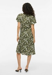 Květinové šaty s krátkými volánkovými rukávy v zeleném a bílém listovém vzoru; ke kolenům, s přiléhavým pasem a měkkou, splývavou tkaninou.