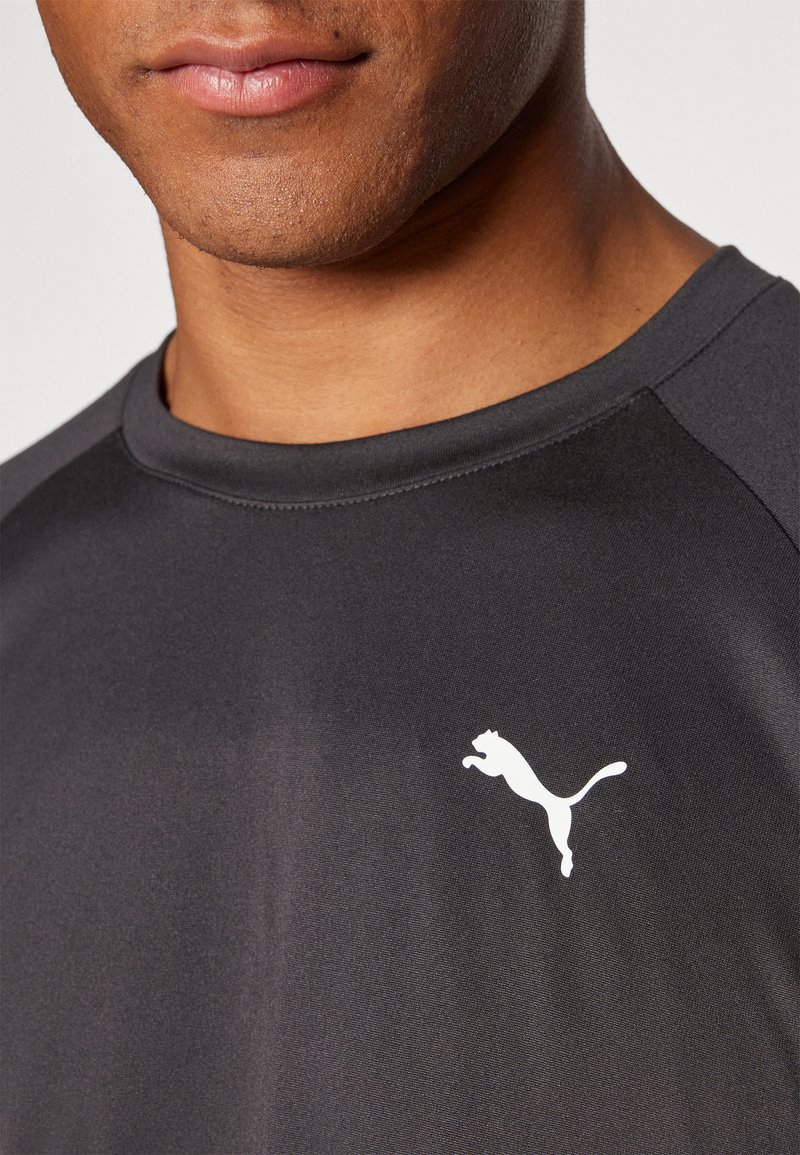 Czarny t-shirt sportowy z okrągłym dekoltem i rękawami raglanowymi. Posiada białe logo skaczącego kota na lewej części klatki piersiowej. Gładka tekstura materiału.