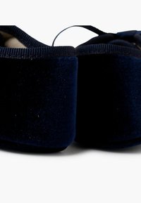 Námořnické modré sametové pantofle s jemnou texturou, zaobleného tvaru a elastickým otvorem pro snadné obutí.