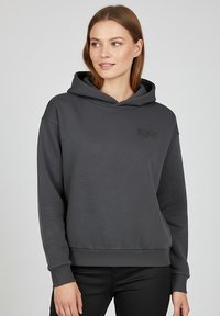 Gray hoodie made of soft fabric with a front kangaroo pocket, ribbed cuffs, and a small embossed text detail on the chest.