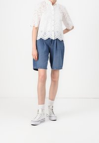 Witte eyelet blouse met korte mouwen en scalloped zoom, gecombineerd met blauwe denim shorts. Draagt witte hoge sneakers en sokken.