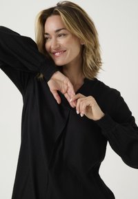Blusa negra con un patrón de diamante texturizado. Presenta un corte holgado, mangas largas con puños elásticos y un detalle de escote en V.