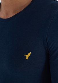 Mørkeblå bomull T-skjorte med rund hals, med en gylden brodert fuglelogo på venstre brystområde.