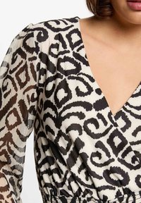Top envolvente de estampado negro y crema con un profundo escote en V, mangas largas de tul y cintura elástica para una silueta ajustada.