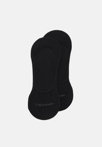 Chaussettes noires de cheville en matériau doux, avec un design sans coutures et un petit logo discret sur la partie inférieure.