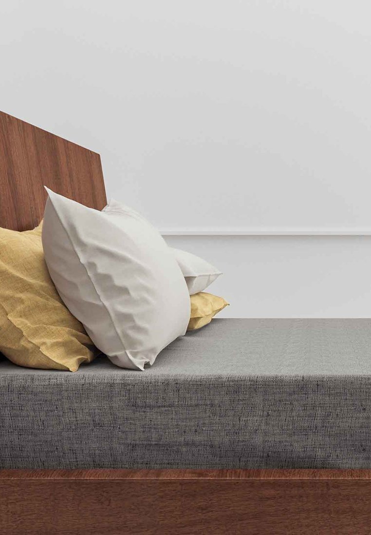 Drewniane łóżko z pochylonym zagłówkiem, szarym materacem tapicerowanym i trzema poduszkami: jedną białą, jedną żółtą i jedną o teksturowanym szarym wykończeniu.