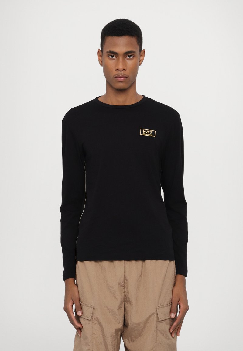 Camisola de manga longa preta feita de algodão. Apresenta um pequeno logótipo dourado no peito, decote redondo e um design ajustado.