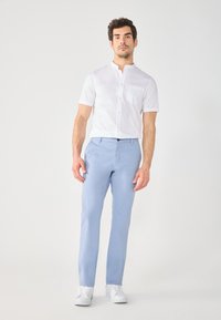 Hvit kortermet skjorte med knappestolpe og krage, kombinert med lyseblå bukser og hvite joggesko. Enkel, skreddersydd design.