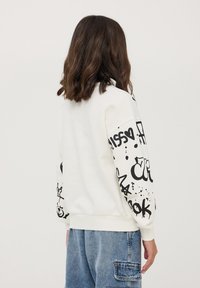 Biała bluza z nadrukiem w stylu graffiti w kolorze czarnym na rękawach, z prążkowanymi mankietami i dołem. Luźny, casualowy krój o miękkiej fakturze.