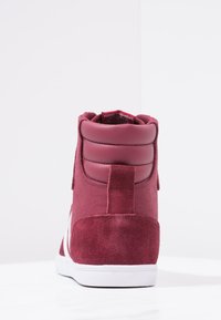 Adidași înalți din material textil și suede maron, cu guler căptușit și talpă din cauciuc alb cu accente contrastante.