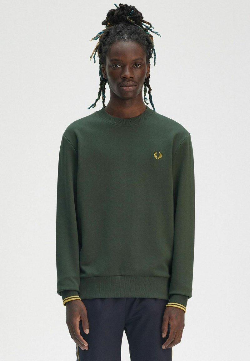 Felpa verde scuro con collo a giro, polsini a costine con dettagli gialli e un piccolo emblema dorato sul lato sinistro del petto. Materiale morbido.