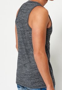 Camiseta sin mangas de color gris, hecha de una tela texturizada, con diseño ajustado y cuello redondeado, que muestra la espalda y la zona de los hombros.
