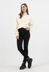 Crème turtleneck trui met volumineuze mouwen, gecombineerd met zwarte high-waisted jeans en zwarte puffer sneakers. Eenvoudig modern ontwerp.