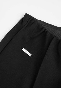 Czarny bawełniany pas z marszczoną teksturą, z przyczepioną srebrną metalową metką z logo, na której widnieje nazwa marki.